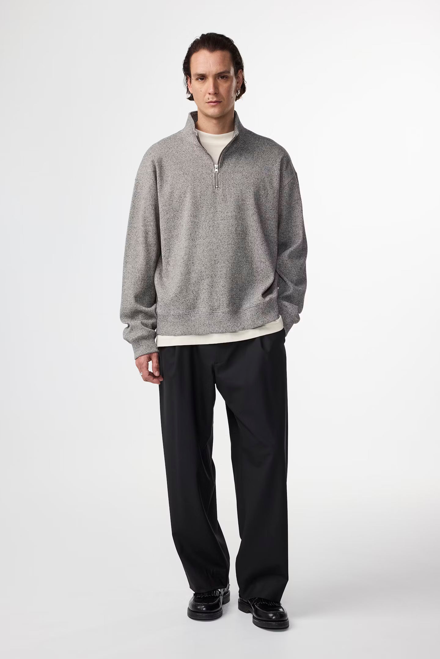 Man wearing a gray sweater and black pants on a white background