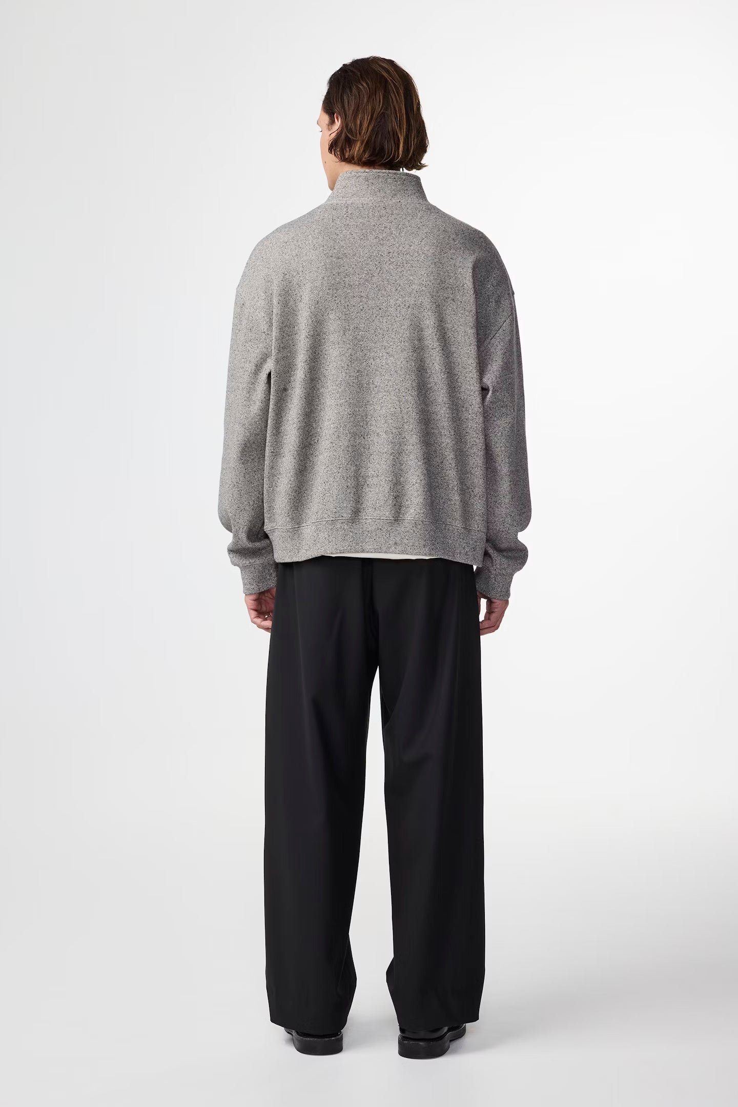Person wearing a gray sweater and black pants on a white background