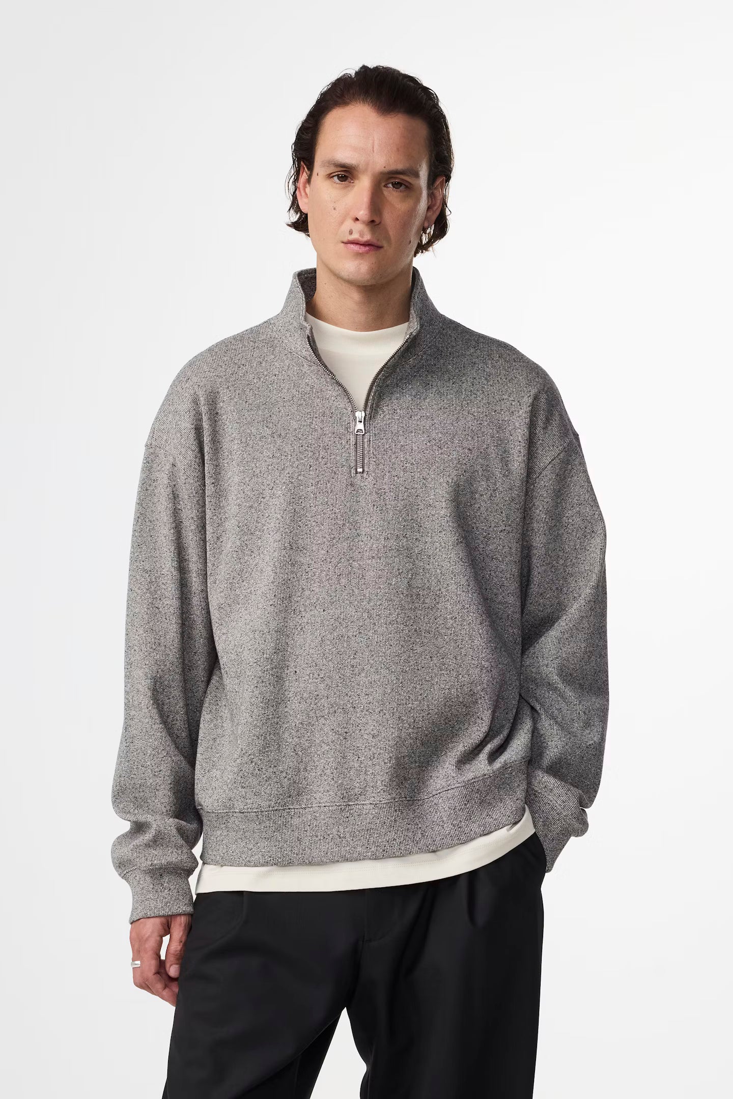 Man wearing a gray zip-up sweater over a white shirt on a white background